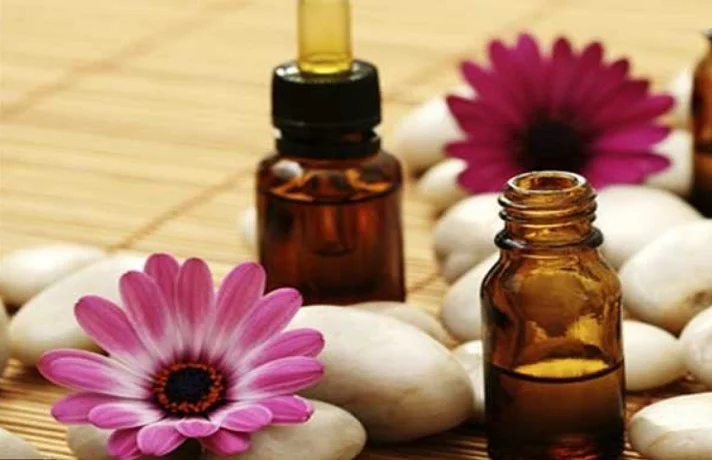 دو شیشه اسانس روغنی در کنار گل های صورتی